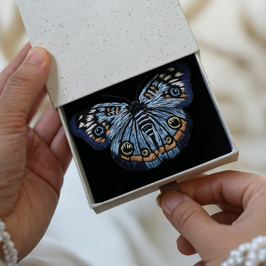 A custom hand-embroidered blue butterfly brooch pin elegantly presented inside a premium textured white keepsake gift box, showcasing its luxury gift-ready packaging.