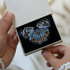 A custom hand-embroidered blue butterfly brooch pin elegantly presented inside a premium textured white keepsake gift box, showcasing its luxury gift-ready packaging.