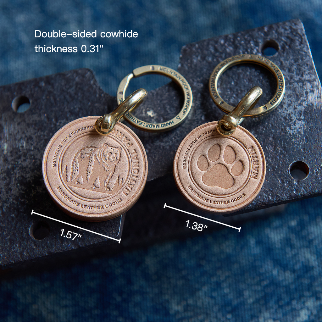 Two bronze keychains with paw and bear designs on a textured surface with measurements.
