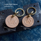 Two bronze keychains with paw and bear designs on a textured surface with measurements.