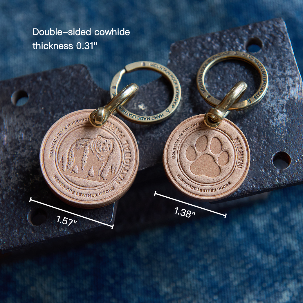 Two bronze keychains with paw and bear designs on a textured surface with measurements.
