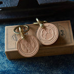 Two leather keychains with paw prints on a cardboard box against a denim background