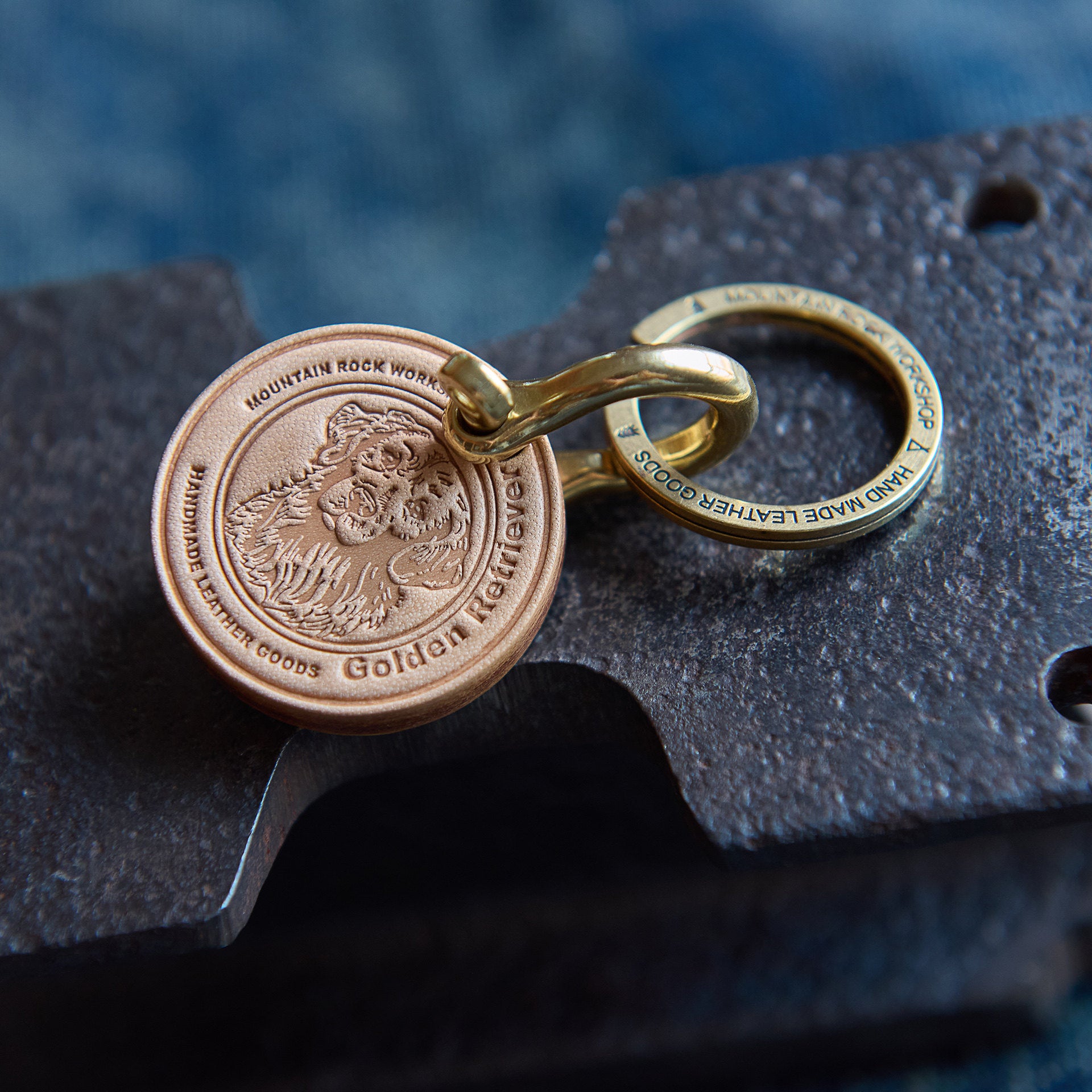 Gold keychain with engraved design on a dark textured surface
