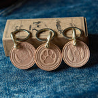 Three bronze keychains with engraved designs on a blue textured surface.