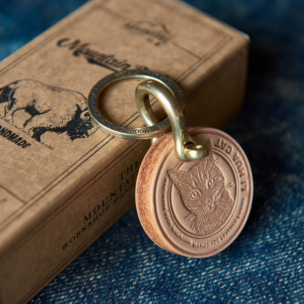Bronze keychain with cat design on a denim surface