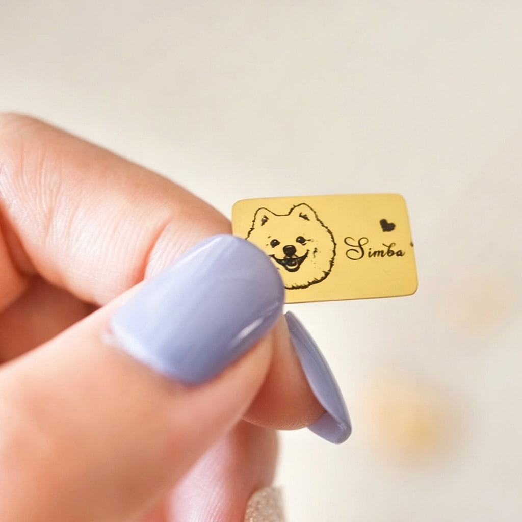 Gold pet tag with a dog illustration and 'Simba' text held by a hand with purple nail polish.