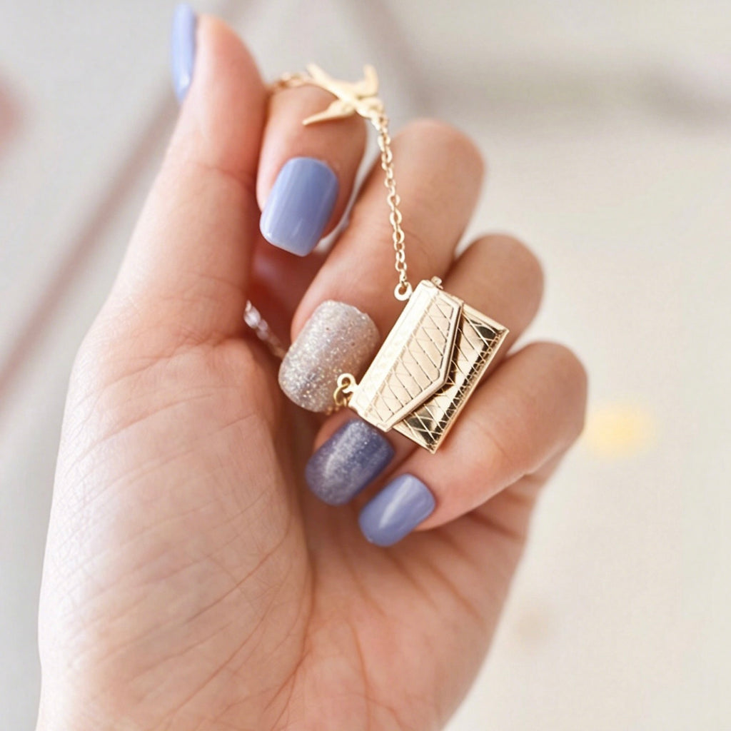 Gold necklace with a pendant held by a hand with purple nail polish on a light background