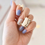 Gold necklace with a pendant held by a hand with purple nail polish on a light background