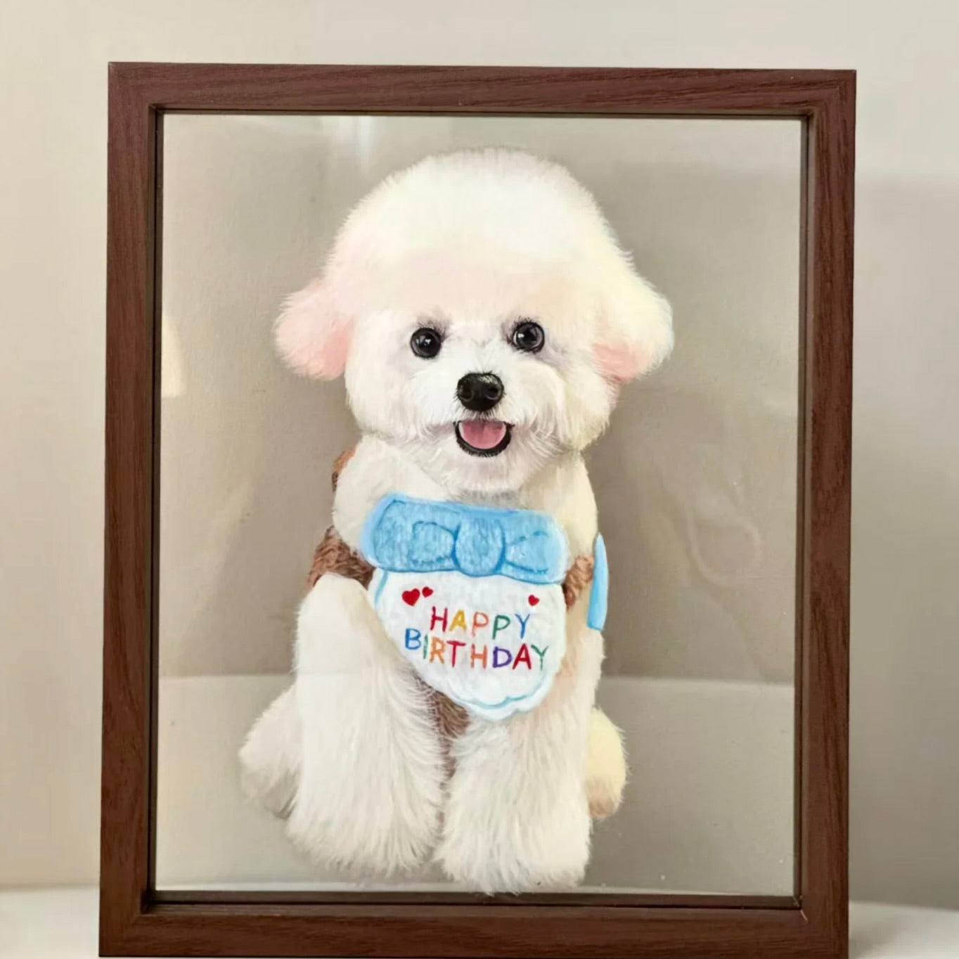 White dog wearing a 'Happy Birthday' shirt in front of a wooden frame.