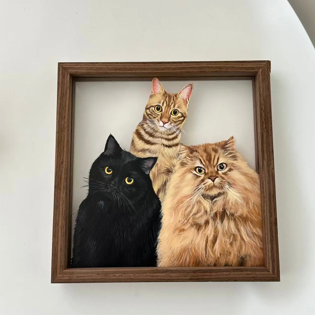 Framed artwork of three cats: a black cat, a tabby cat, and a long-haired cat, on a white wall.