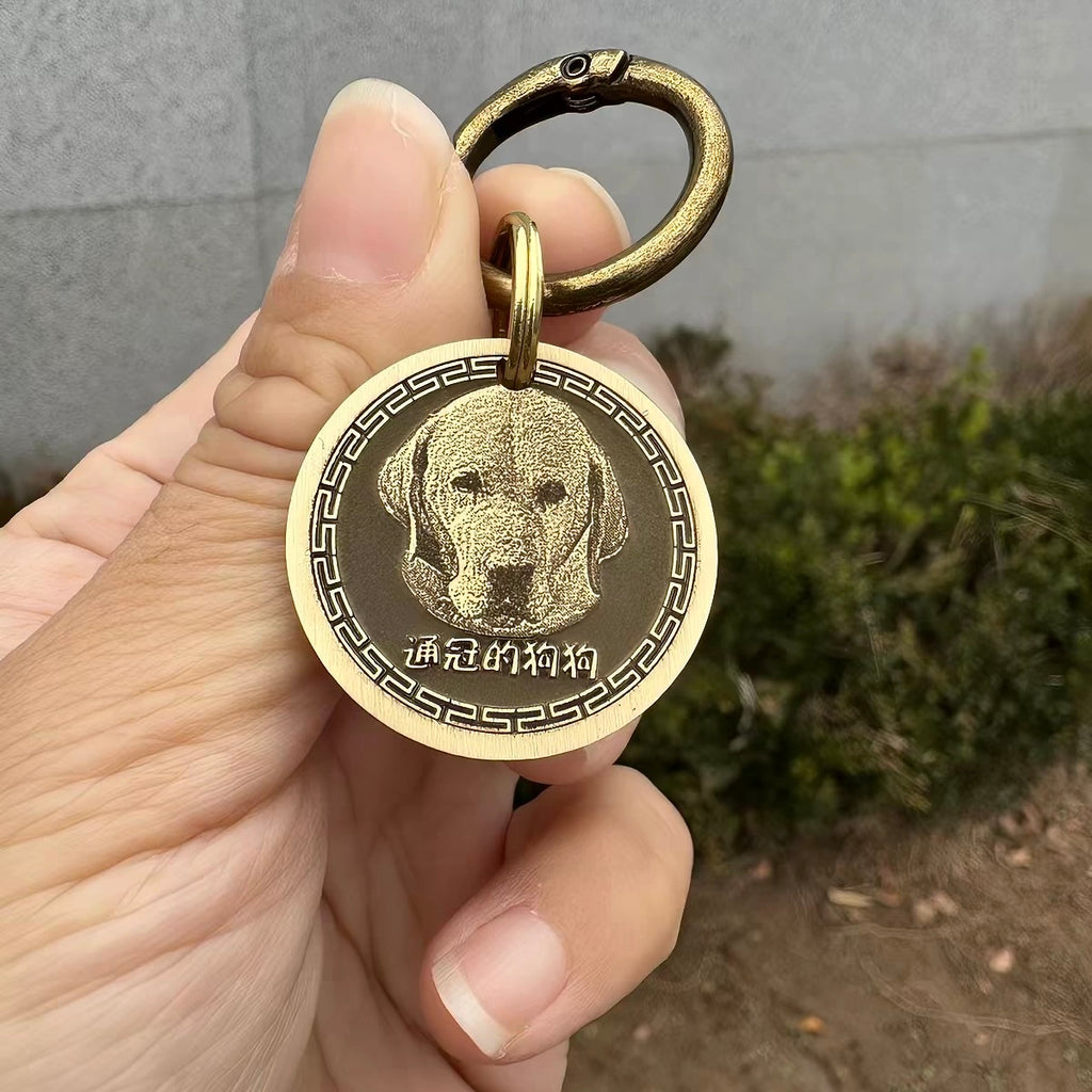 Gold dog tag with a dog's face on it held by a hand against a neutral background