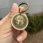 Gold dog tag with a dog's face on it held by a hand against a neutral background