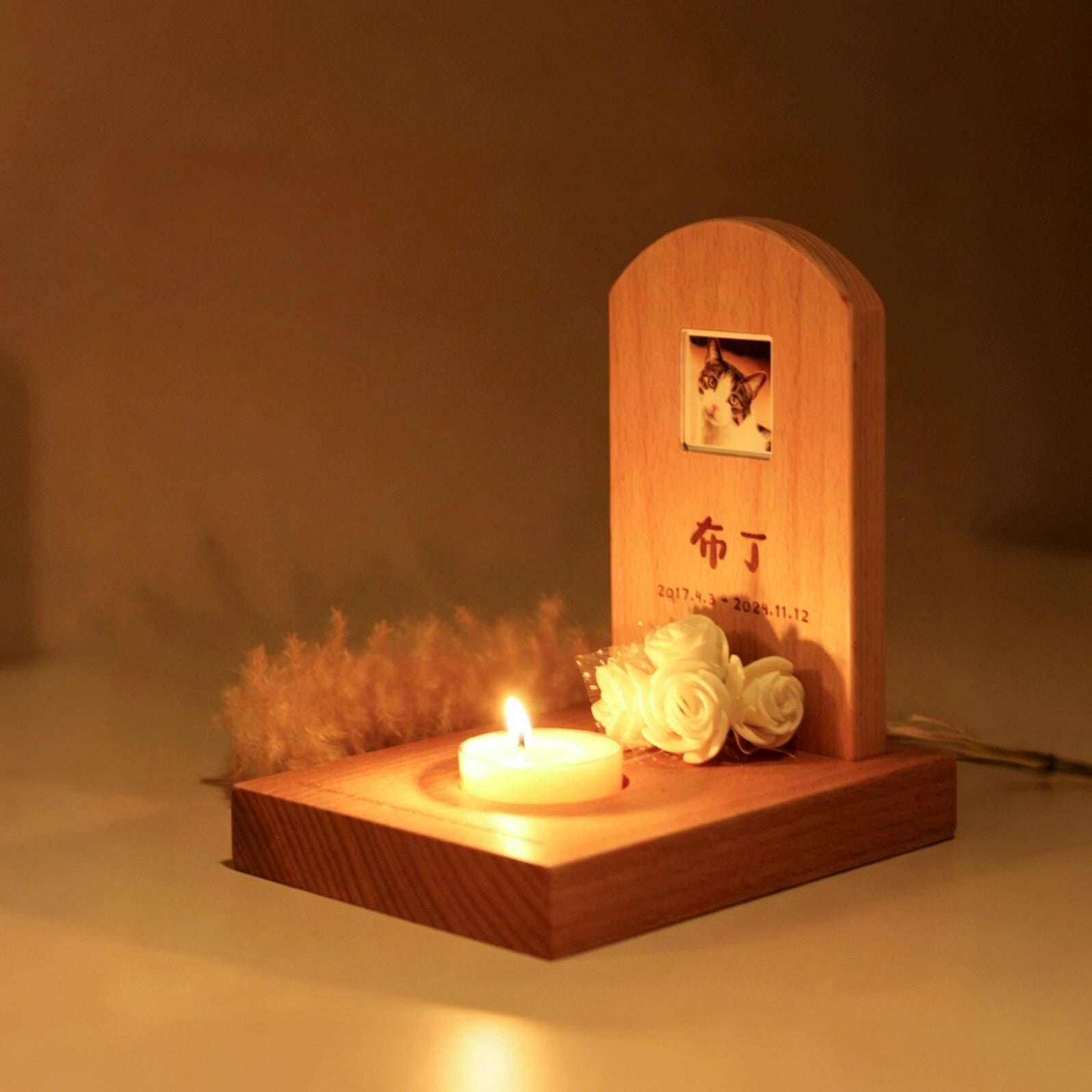 Wooden memorial with candle, flowers, and photo on a dark background