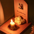 Memorial wooden plaque with a candle and flowers for a pet named 'Pudding'.