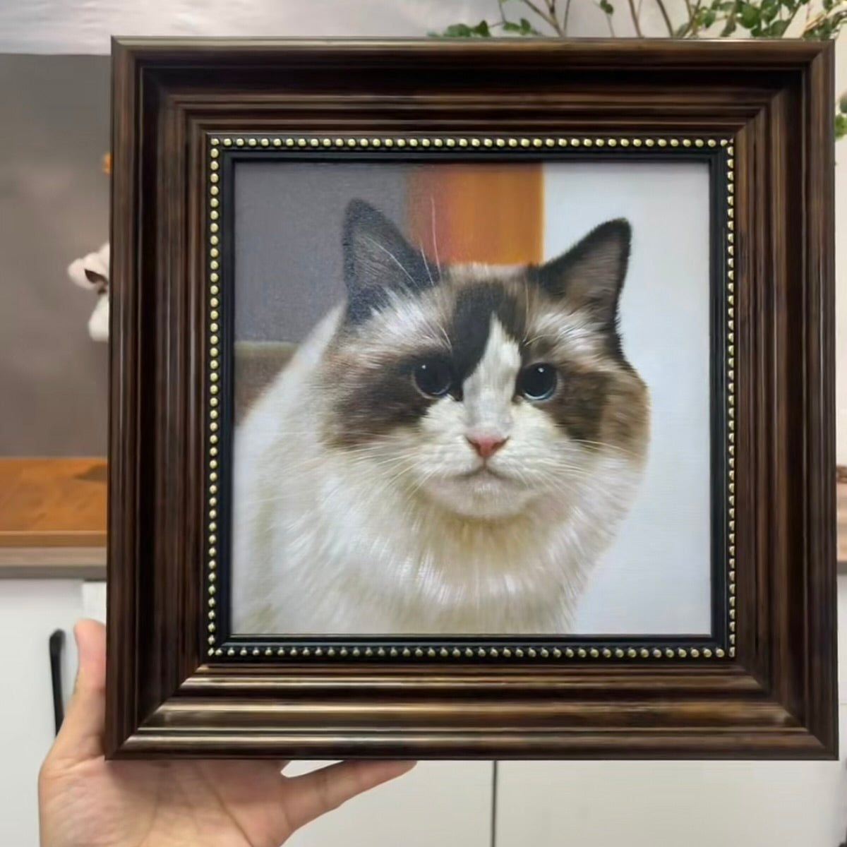 Framed portrait of a cat with a wooden frame held by a hand.