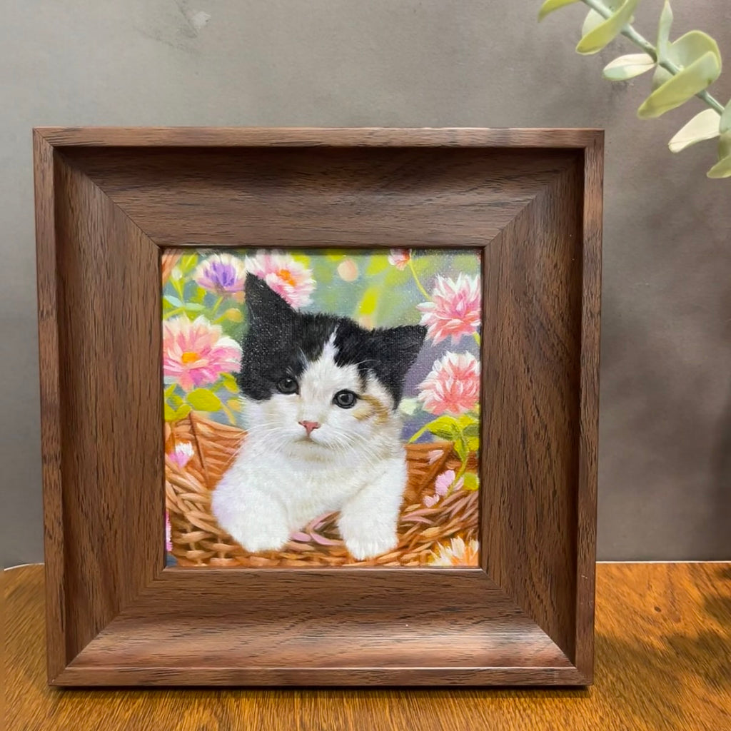 Framed artwork of a cat in a basket with flowers on a wooden surface