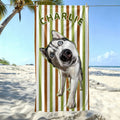 A green and brown striped custom pet portrait beach towel featuring a Siberian Husky and the personalized name Charlie, hanging on a sunny beach.