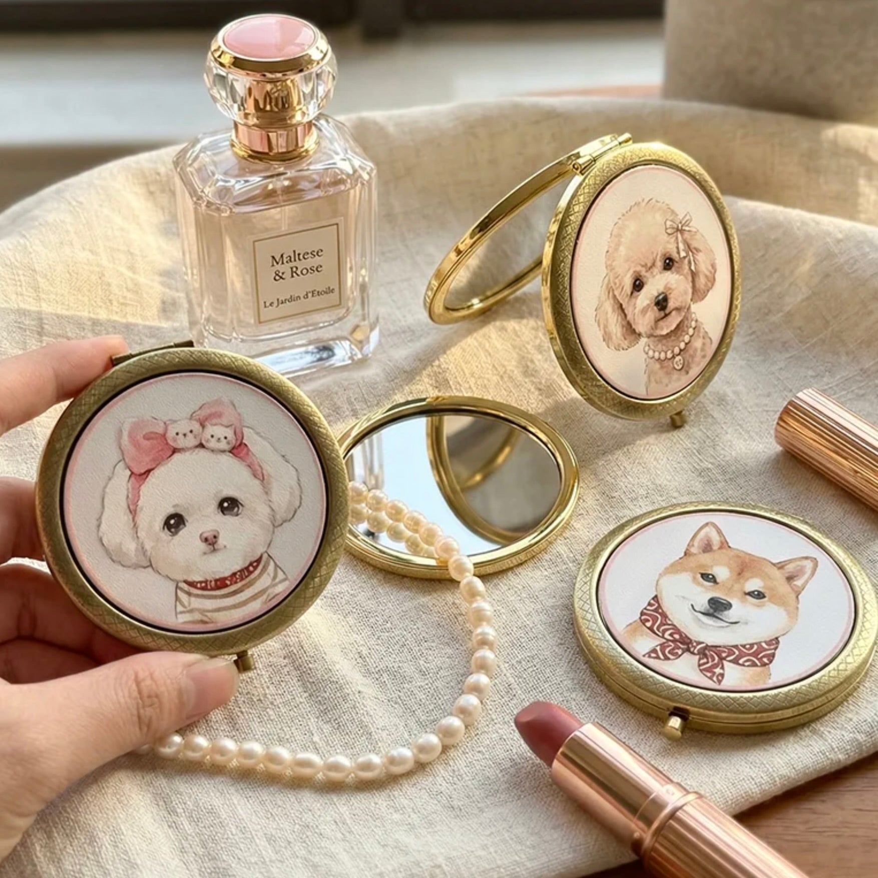 Compact mirrors with dog illustrations on a textured surface with a perfume bottle and makeup items.