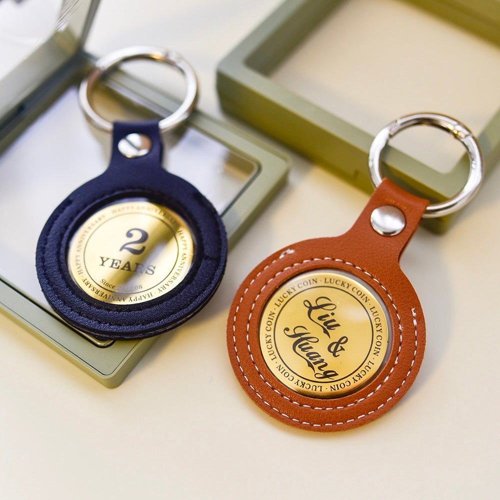 Two round keychains, one navy and one brown, with gold accents on a light background.