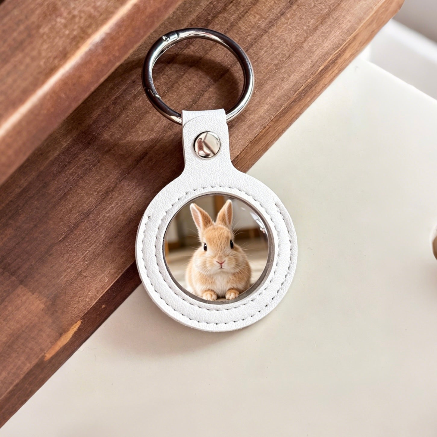 Keychain with a round white leather tag featuring an image of a rabbit on a wooden surface.