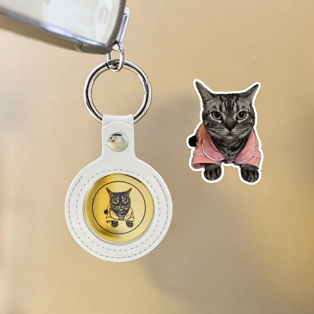 White keychain with gold coin featuring a cat illustration, next to a sticker of a cat wearing a pink sweater on a beige background.