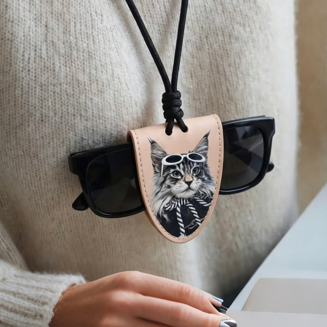 Sunglasses with a leather case featuring a cat design, held by a person wearing a beige sweater.