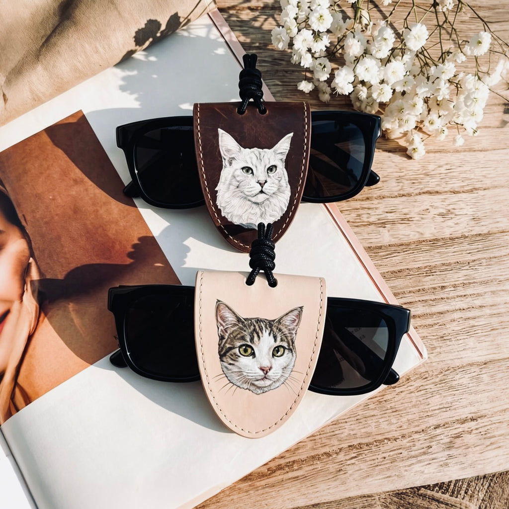 Sunglasses with cat-themed cases on a wooden surface with flowers and a magazine.