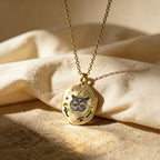 Gold necklace with a pendant featuring a cat design on a beige fabric background