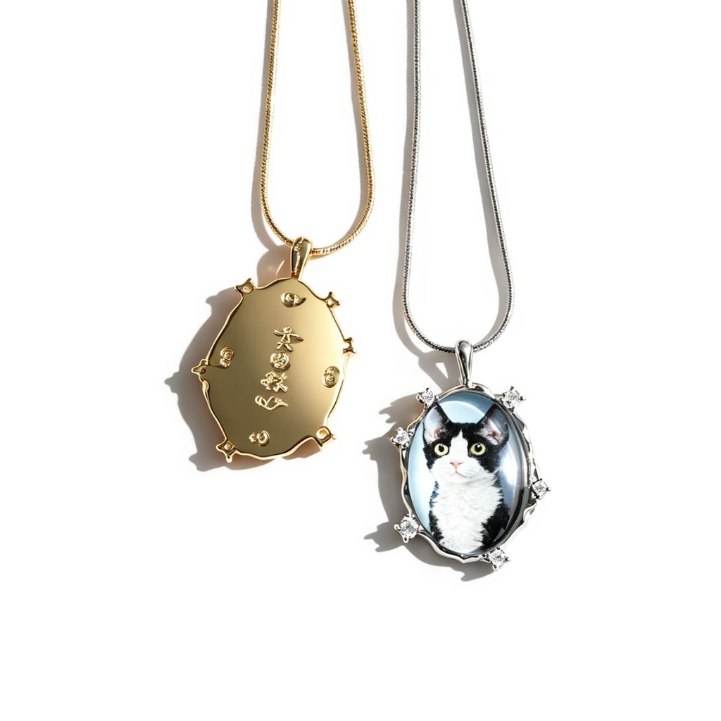 Two necklaces with pendants, one gold and one with a cat design, on a white background.