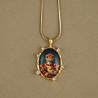 Gold necklace with a pendant featuring a painted design of a snake and a person, on a beige background.