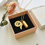Gold necklace with a pendant in a box on a light surface with dried flowers.