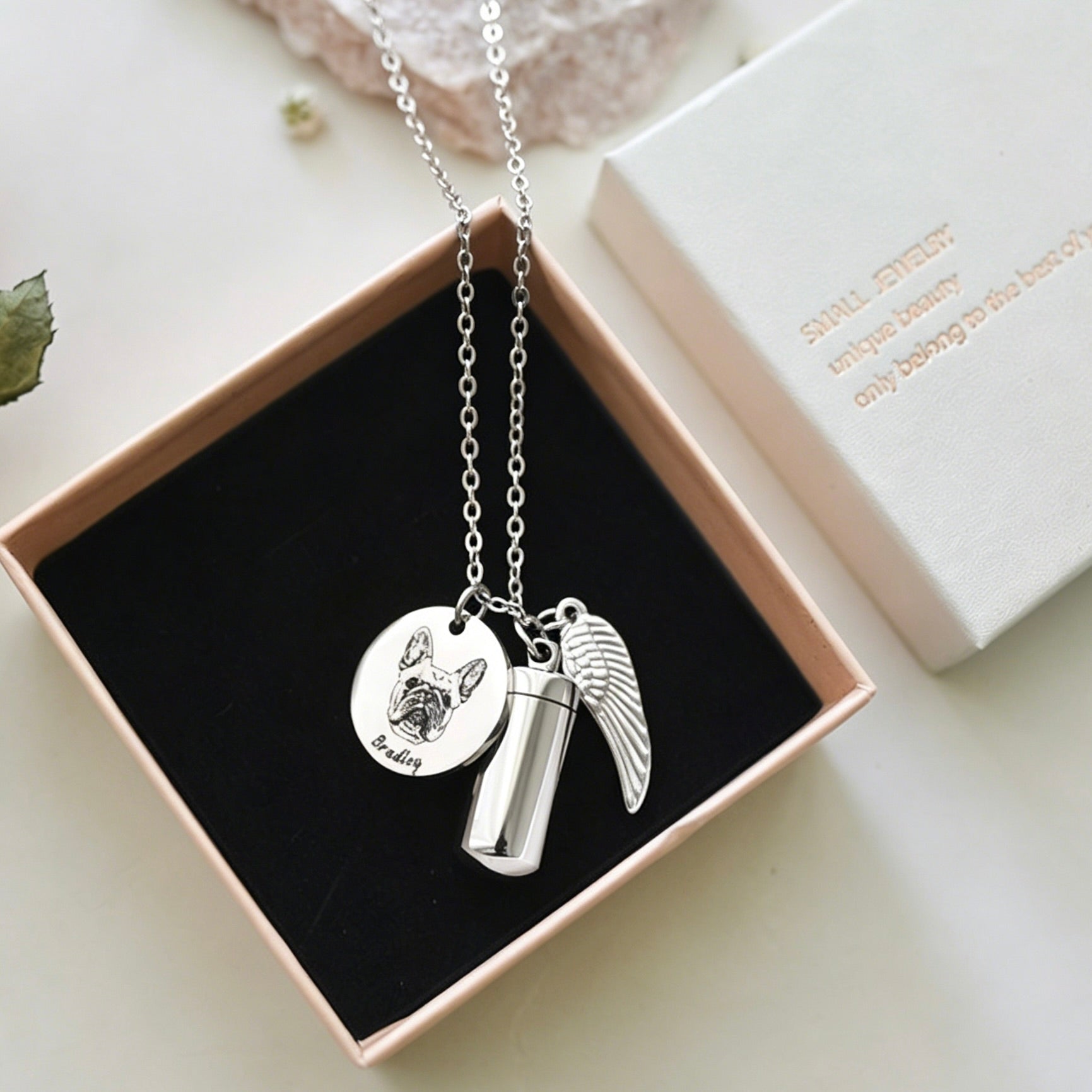 Silver necklace with pendant and engraved disc in a box on a light surface