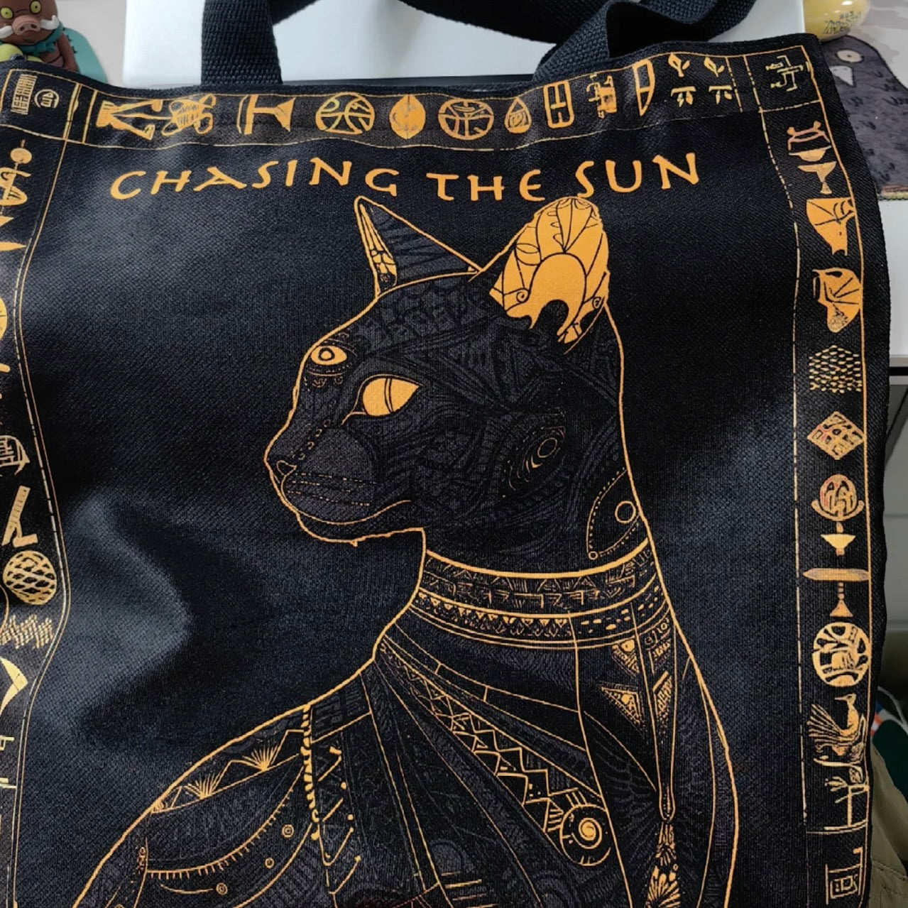 Black tote bag with gold Egyptian-themed design and 'Chasing the Sun' text.