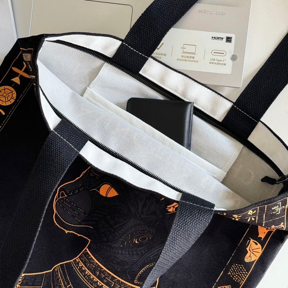 Black tote bag with cat design and white interior, containing a phone and documents.