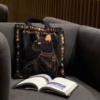 Tote bag with cat design and 'Chasing the Sun' text on a gray couch next to an open book.