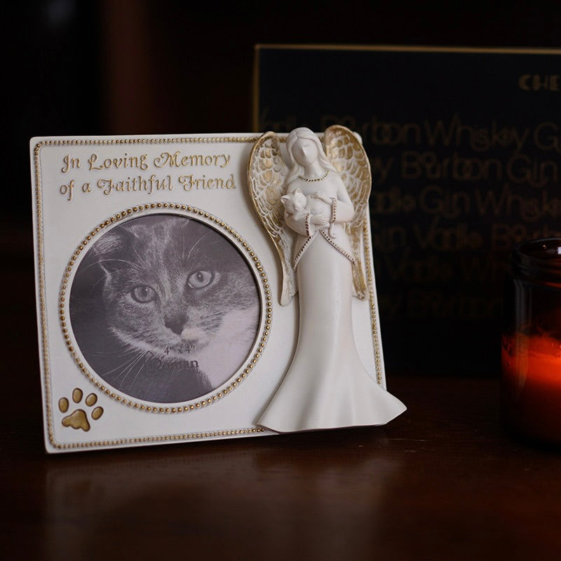Memorial photo frame with angel design and cat's face, placed on a dark surface.