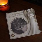 Memorial plaque with a cat's photo, angel figure, and 'In Loving Memory' text on a wooden surface with a candle.