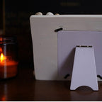 White photo frame with a small stand on a dark surface, candle in the background