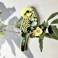 Decorative brooch shaped like a parakeet with gemstones on a branch with leaves.