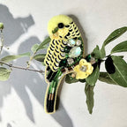 Decorative brooch shaped like a parakeet with gemstones on a branch with leaves.