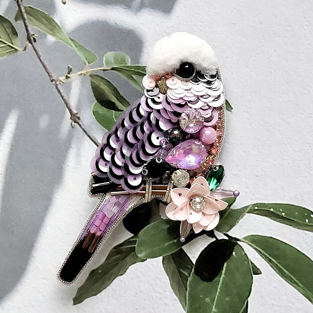 Decorative bird-shaped object with sequins and gemstones on a leafy branch.