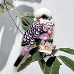 Decorative bird-shaped object with sequins and gemstones on a leafy branch.