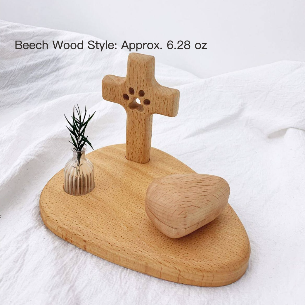 Wooden cross and heart-shaped object on a wooden base with a small plant, on a white fabric background.