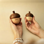 Two hands holding wooden acorn-shaped objects with 'Leo' engraved on a beige background