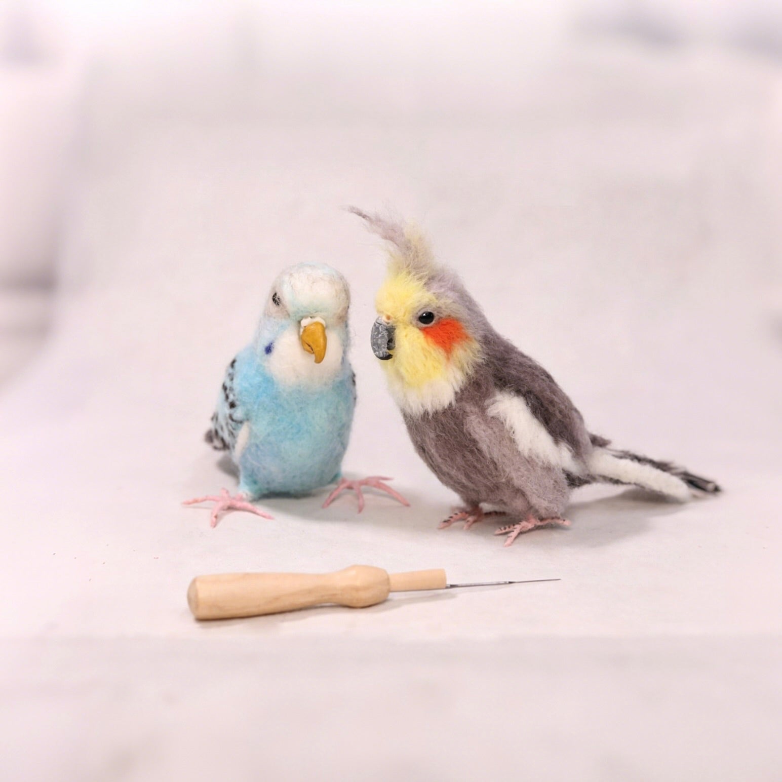 Two toy parakeets and a wooden perch on a light gray background