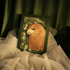 Framed artwork of a fluffy creature with flowers on a draped surface
