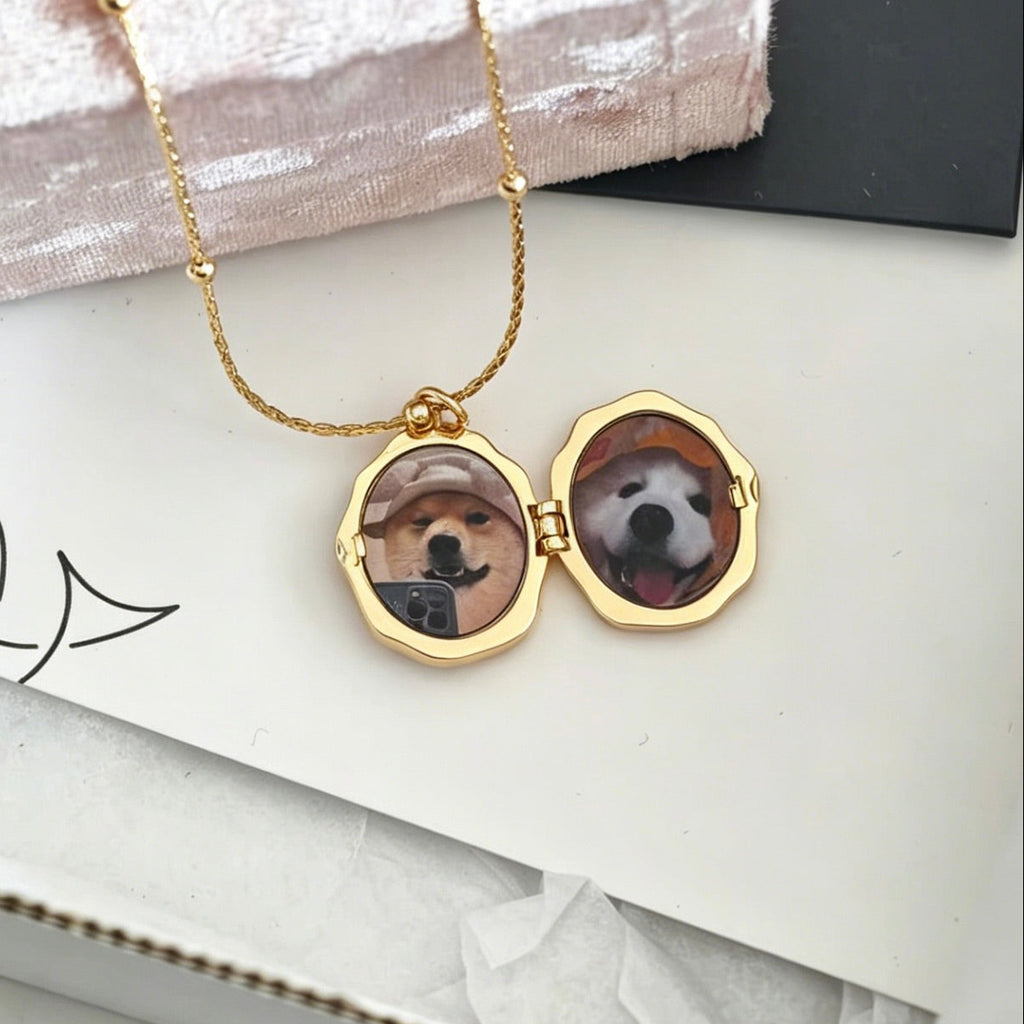 Gold necklace with a locket featuring two dog portraits on a white surface.