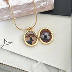 Gold necklace with a locket featuring two dog portraits on a white surface.