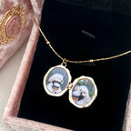 Gold necklace with locket pendant featuring images of a dog on a black velvet surface.