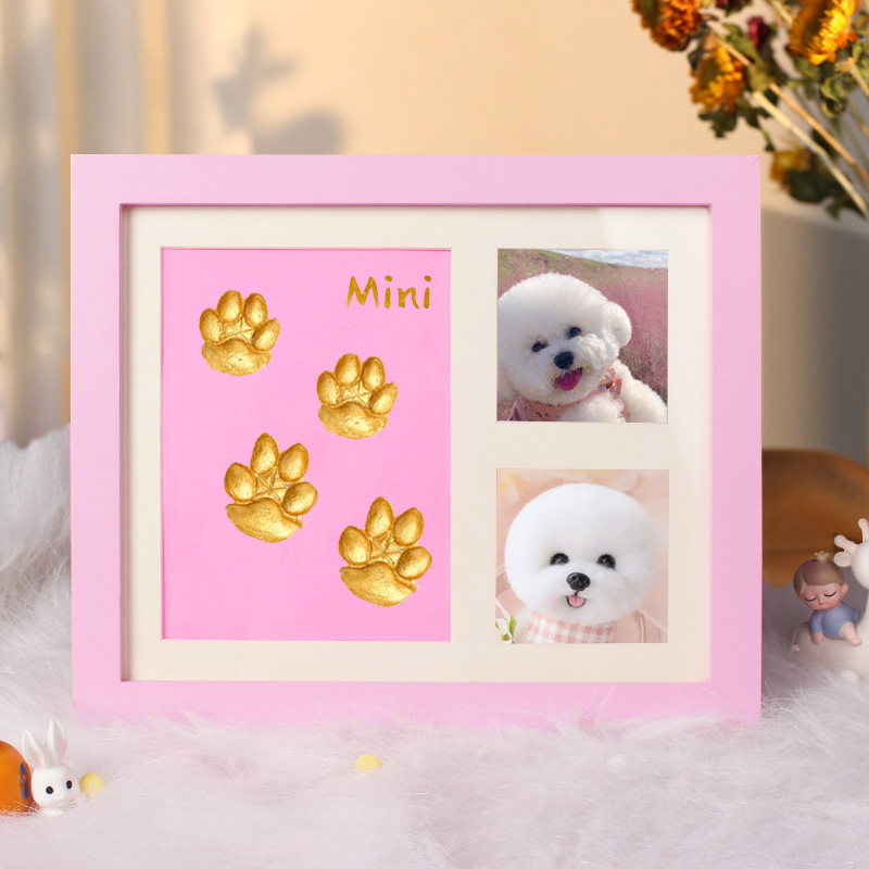 Pink photo frame with gold paw prints and a small dog's face, on a soft surface with blurred background.